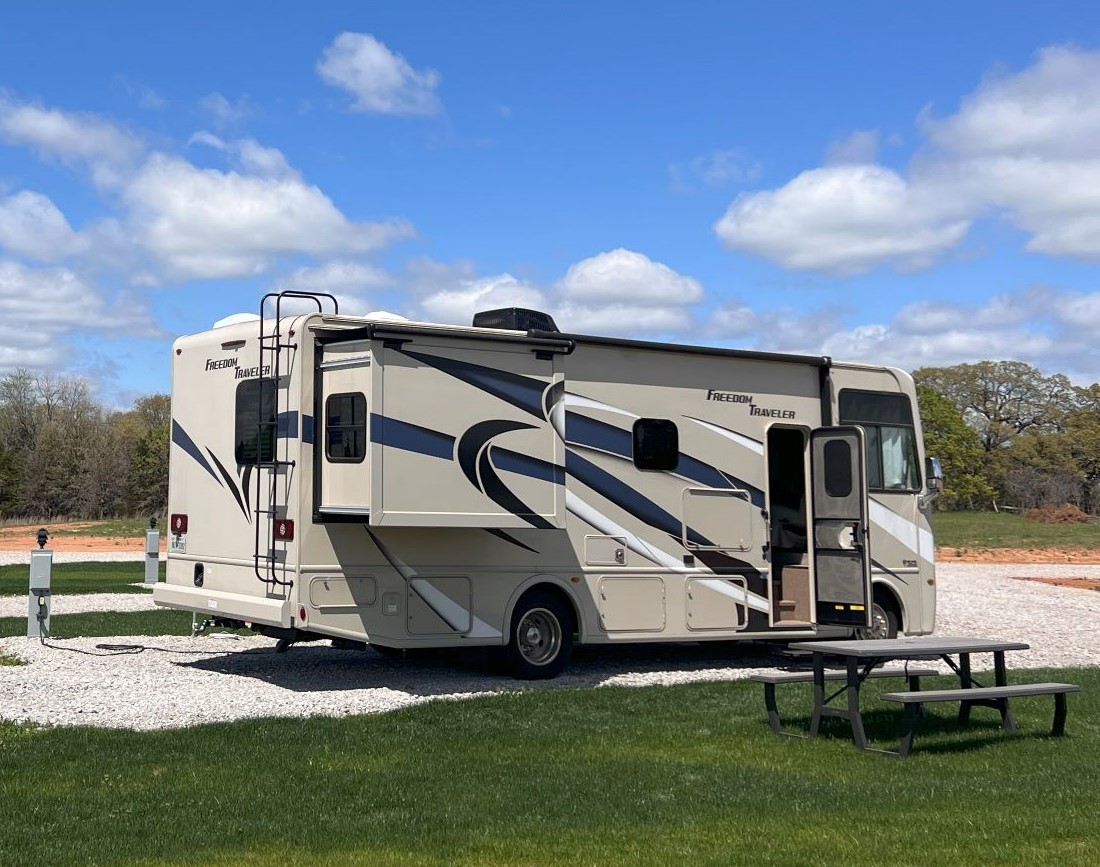 Motorhome RV parked at full-hookup pull-thru site with picnic table at Roadrunner Ranch